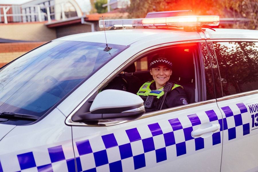 Victoria Police woman smiling while she sits in passenger seat of police car.